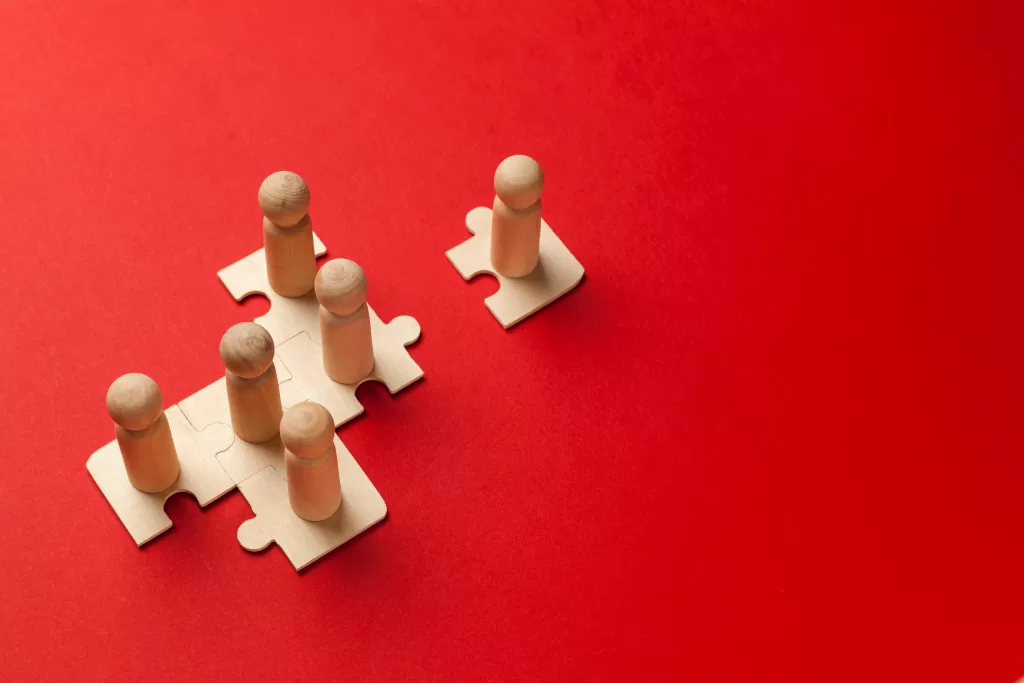 Wooden figures on puzzles on red background as a symbol of team building. Organization group people in business. Cooperation and partnership.